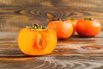 Half ripe persimmon on a brown wooden background, close-up