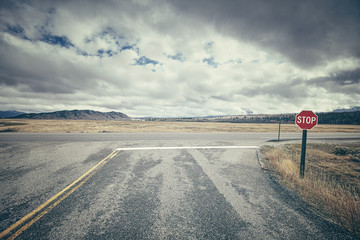 Retro stylized road intersection with stop sign on a cloudy day, conceptual picture, USA.