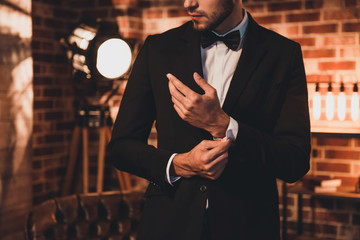 close up of stylish man in black suit fastening cufflinks in lof