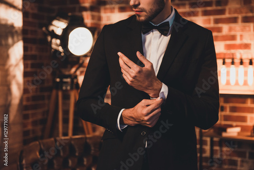 Valokuva  Close up of stylish man in black suit fastening cufflinks in lof