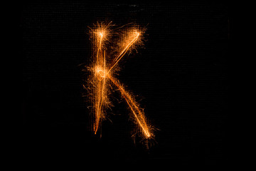 Letter K made of sparklers on black