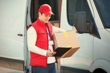 Wall Mural - Young male courier with clipboard and parcel near delivery service van