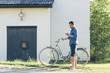 © FOLIO - Sweden, Smaland, Mortfors, Man standing by house with bicycle and using phone