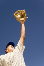 Low Angle View Of Baseball Player Trying To Catch The Ball Against Blue Sky