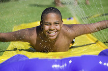 Boy (10-12) Sliding On Water Slide Front View Portrait.