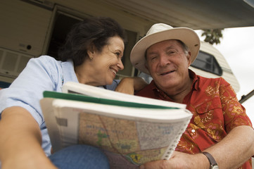 Happy senior couple holding map book with caravan in the background