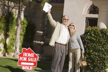 Excited couple standing in front of house with a For Sale Sold sign