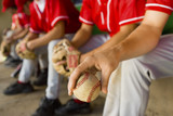 Low section of baseball team mates sitting in dugout with player holding a ball in foreground