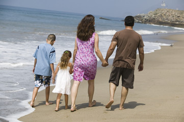 Rear view of a family holding hands and walking at water's edge on the beach