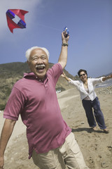 Wall Mural - Cheerful Asian couple flying kite on the beach