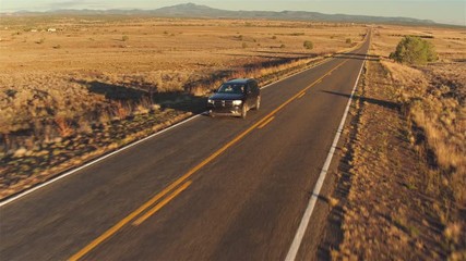 Wall Mural - AERIAL: car driving along empty countryside road at sunset