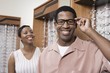 © moodboard - Portrait of happy African American man trying on glasses with woman smiling in the background