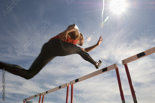 Cuadros en Lienzo Low angle view of a male athlete jumping hurdle against the sky