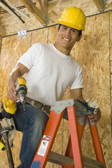 Portrait of a smiling middle aged construction worker on ladder holding a power tool