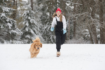 Happy young girl running in the snow with her golden retriever d