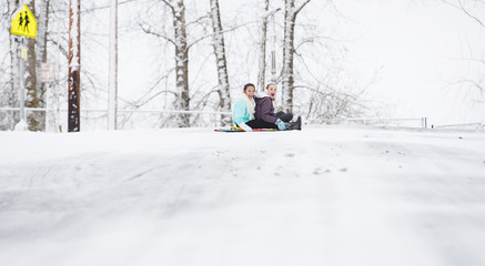 Wall Mural - Two young girls sledding down hill in ice and snow