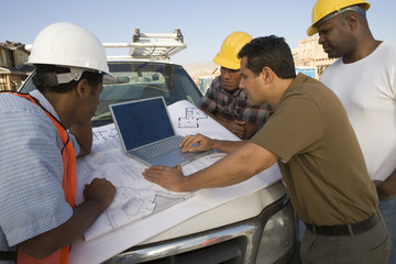 mature man with team of architects using laptop at construction site