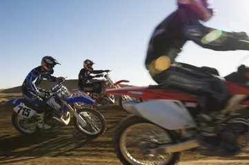 Wall Mural - Three motocross racers racing in desert against blue sky