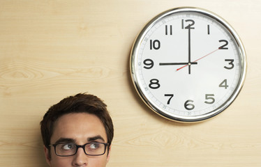 Wall Mural - Headshot of young businessman wearing spectacles looking at clock on wooden wall in office