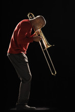 Side View Of An African American Man Playing The Trombone Against Black Background