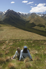 Wall Mural - Rear view of a man and woman sitting on grass and looking at mountains