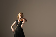 Young Woman Playing The Violin Against Gray Background