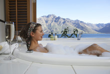 Side View Of A Young Woman Taking Bubble Bath With Mountain Lake Outside Window