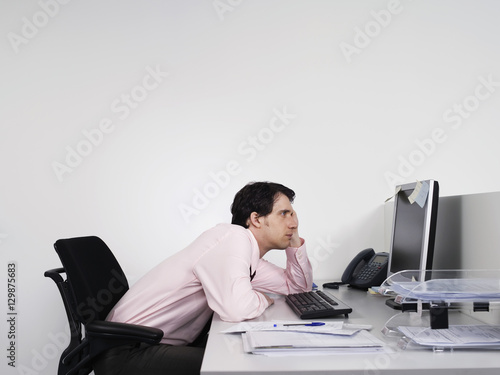 side view of a bored male office worker looking at notes on computer