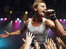 Young Man Singing On Stage In Concert With Adoring Fans Reaching Towards Him