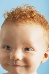 Wall Mural - Closeup of redhead cute baby with pursed lips isolated on blue background