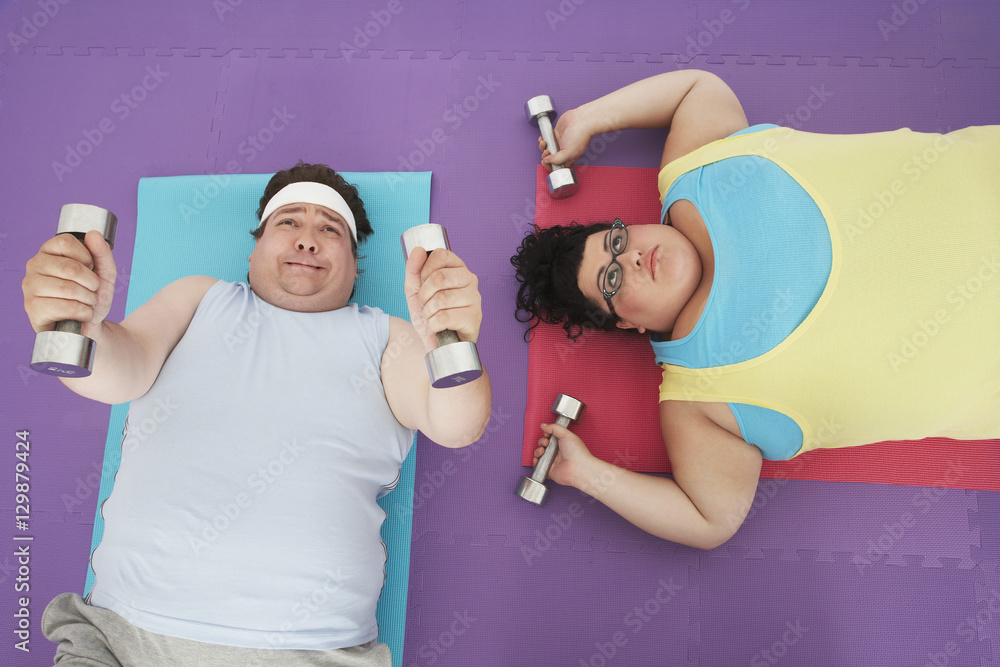 Overhead view of an overweight man and woman lifting dumbbells 