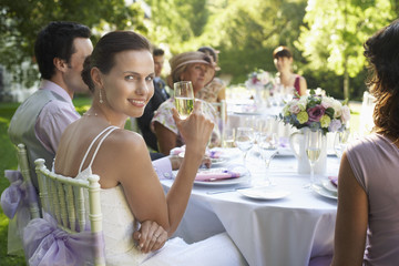 Portrait of beautiful bride holding champagne flute while sitting with guests at wedding table