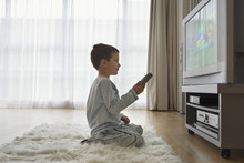 Side View Of A Boy Sitting On Floor And Watching Cartoons In Television