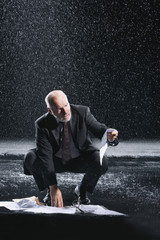 Middle aged businessman picking up soaked documents during downpour