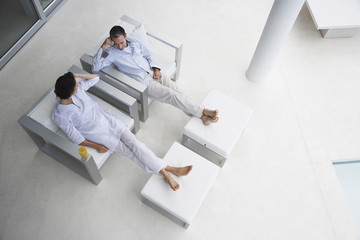 High angle view of happy couple sitting on armchairs with feet on foot stools in modern house