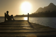 Side View Of Man Sitting On Dock By Lake Enjoying Sunset