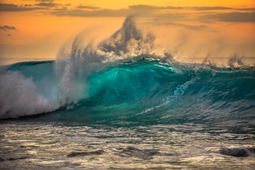 Fototapete - Green blue ocean splashing wave in front of orange sunset sky background