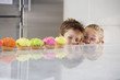 Young girl and boy peeking over counter at row of cupcakes