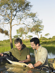 Wall Mural - Two male friends reading map on bonnet against the lake