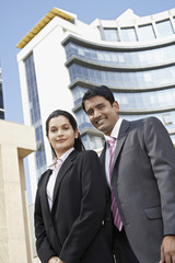 Wall Mural - Low angle view of confident businesswoman and businessman standing in front of building