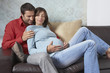 © moodboard - Young man sitting with pregnant woman on couch in living room