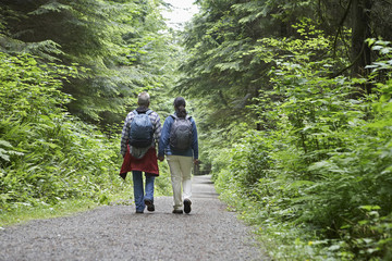 Full length rear view of a couple walking on forest road amid lush trees