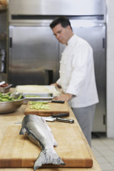 Wall Mural - Side view of a cropped male chef in kitchen with focus on salmon in foreground