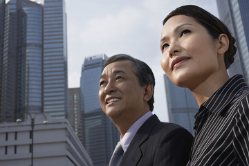 happy businesswoman and businessman looking away against buildings