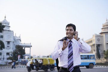 Wall Mural - Happy young businessman using cell phone on city street