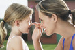 Closeup side view of mother applying sunscreen to smiling daughter's nose outdoors