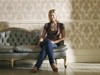 Full length portrait of a young woman sitting on sofa against wallpaper