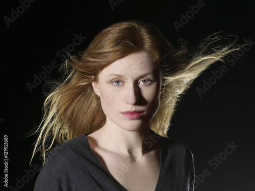 Fotografia, Obraz Closeup of beautiful young woman with windswept hair looking at camera on black