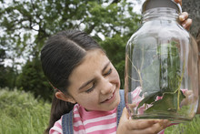 Happy Little Girl Examining Stick Insects In Jar Outdoors