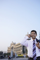 Wall Mural - Happy young businessman using cell phone on city street